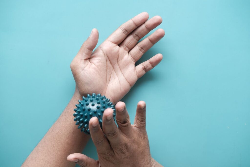 Close-up of hands using a spiky massage ball for therapy against a blue backdrop.